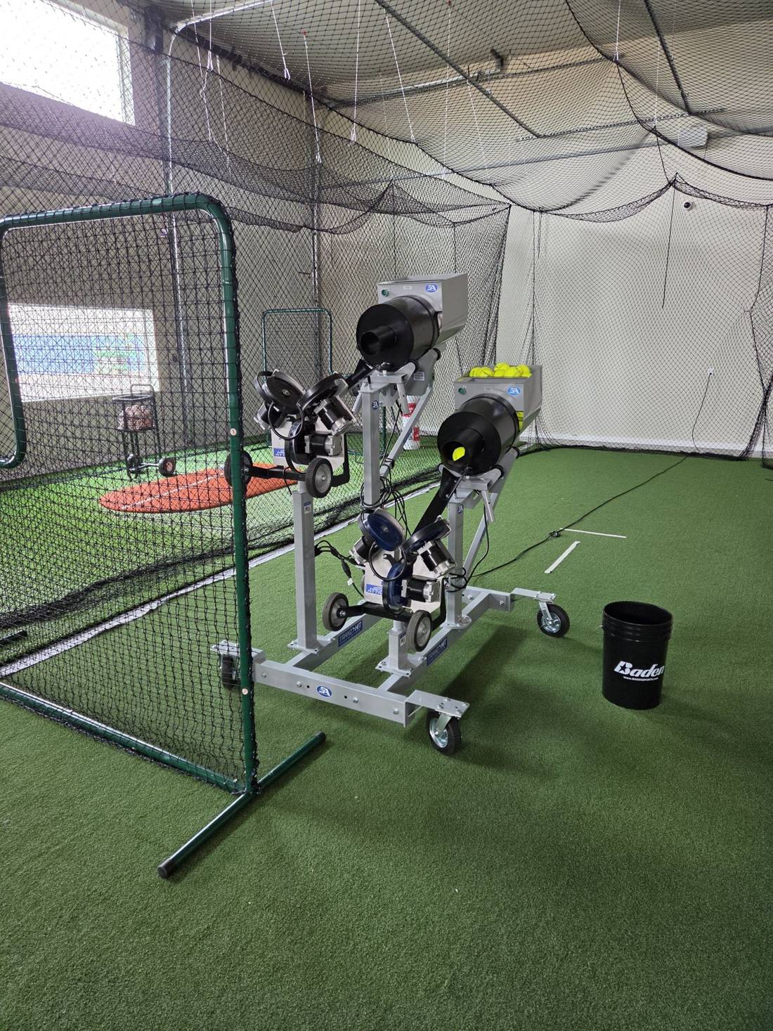 Two Hack Attack pitching machines with automatic ball feeders and a protective screen on the turf